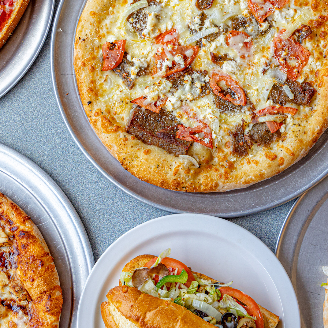 listing5 Pizzas and a sub sandwich on plates.